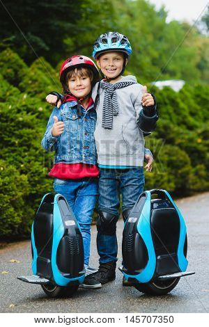 Happy kids standing near mono-wheel hoverboard or gyroscooter outdoor.