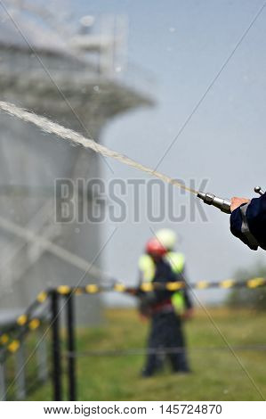 Firefighter holding high pressure water hose extinguishing a fire started near a petrol storage tank