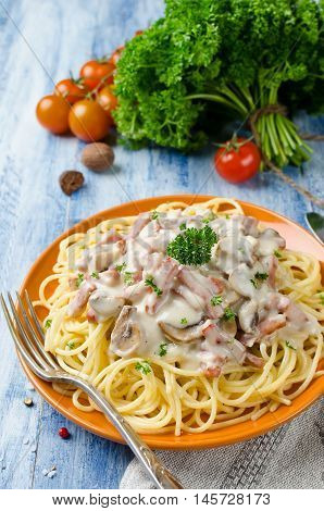 Spaghetti with Bechamel sauce mushrooms and bacon on a wooden table