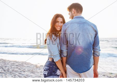 Beautiful young woman holding her boyfriend hand who standing backwards at the beach