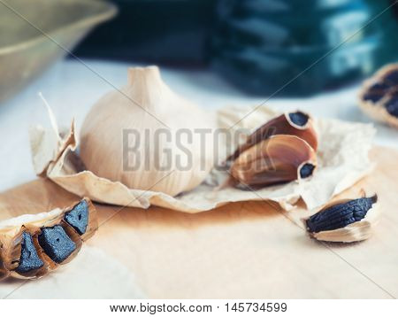 Black Garlic background in a soft focus showing Black garlic glove cut in half on a wooden board . room at base for copy space and text.
