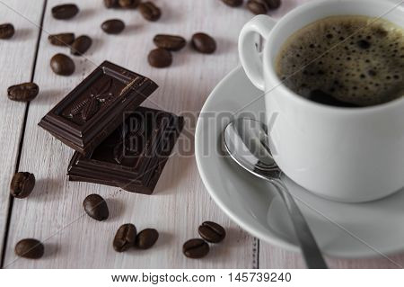 Two pieces of dark chocolate a cup of coffee and coffee beans