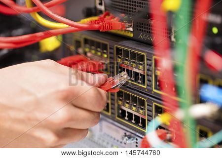 IT technician or engineer connects a gigabit network cable into switch in datacenter