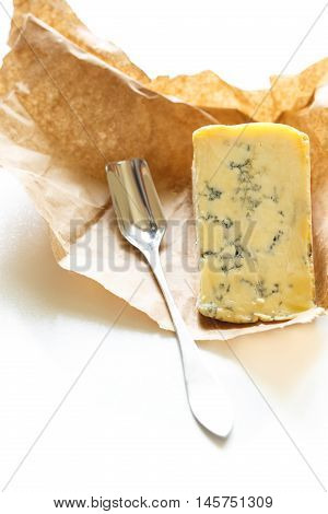 Slice of blue Stilton cheese and stilton spoon on a white background