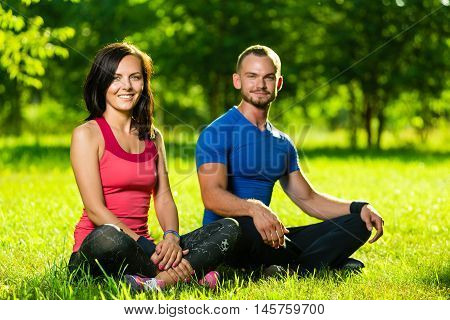 Young man and woman doing yoga in the sunny summer park. Couples Yoga on green grass outdoor.