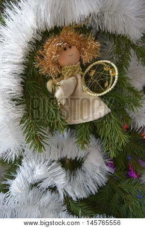 Christmas toy in the form of an angel. The toy is located on a fir-tree. An angel in gold clothes. The angel holds a psaltery.