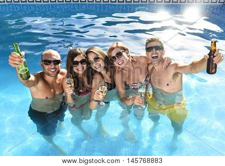 group of friends young happy attractive men and women in bikini having bath at hotel resort swimming pool drinking beer bottle having fun smiling playful in boys and girls summer party and holidays