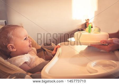 Happy little child looking at birthday cake with burning candle in his first happy birthday