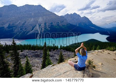 Woman meditating on cliff above Peyto lake in Rocky Mountains. Banff National Park. Alberta. Canada.