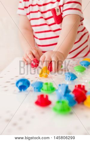 Closeup of child's hand taking bright mosaic parts. Playing and learning colors at home. Toddler boy in a striped shirt playing with colorful constructor details. Activities with children
