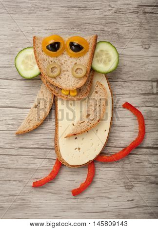 Monkey made of bread cheese and vegetables on wooden background