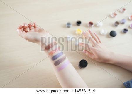 Female hand with colorful eyeshadow smears, visagiste pov. Makeup artist testing colors of decorative cosmetics, top view on swatches