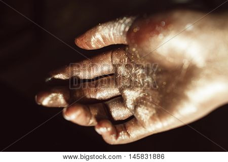 Beautiful hand in golden paint on black background close up. Gilded human palm, ceremonial greasepaint