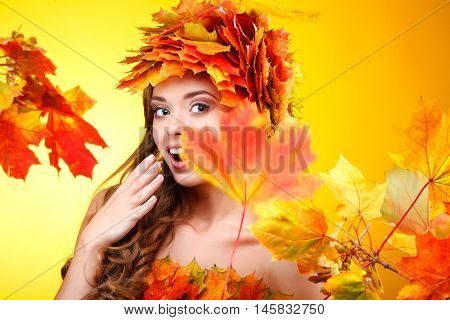 Close-up portrait of beautiful young  girlin in a chaplet from varicoloured autumn leaves on a yellow background