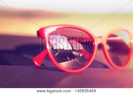 Red sunglasses on the car dashboard with reflection of the sun. Soft focus. Toned image. Blurred effect