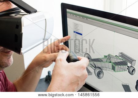 Male engineer working on computer creating a racecar using VR virtual reality glasses and controller.