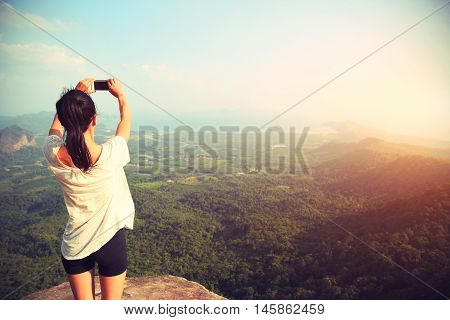 young asian woman taking photo with smart phone at mountain peak cliff