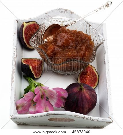 Delicious Homemade Fig Jam in Glass Kremanka with Fresh Fig Fruits and Flowers in White Wooden Tray isolated on White background