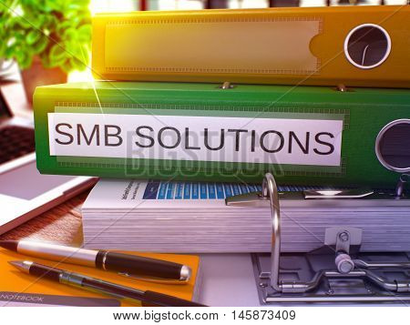 Green Office Folder with Inscription SMB - Small Business Solution - Solutions on Office Desktop with Office Supplies and Modern Laptop. SMB Solutions Business Concept on Blurred Background. 3D.