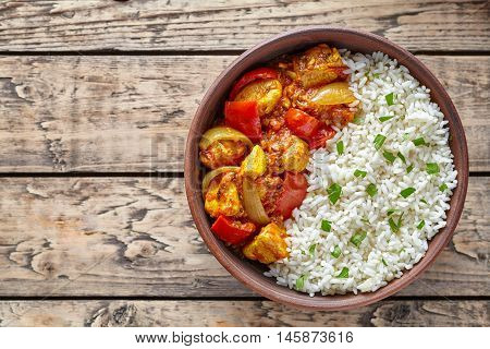 Chicken jalfrezi Indian spicy curry chilli meat with basmati rice and vegetables healthy dietetic asian food in clay dish on vintage table background.