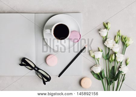 Morning cup of coffee, empty notebook, pencil, glasses, white flowers and cake macaron on light table top view. Beautiful breakfast. Flat lay.