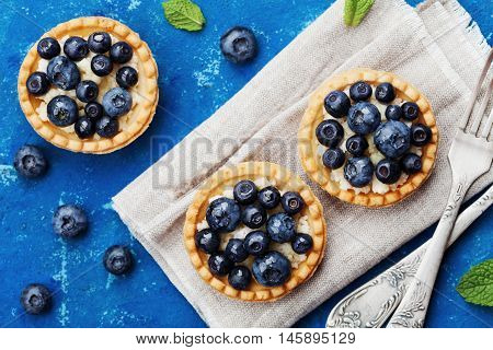 Tartlets with blueberries bilberry ricotta and honey syrup on vintage background top view. Delicious dessert. Flat lay styling.