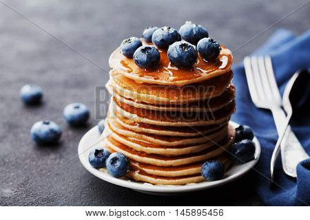 Stack of baked american pancakes or fritters with blueberries and honey syrup on rustic black table. Delicious dessert for breakfast.