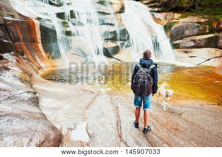 Traveler with his dog. Young man is looking on Mumlava waterfalls in Krkonose National Park Czech Republic.