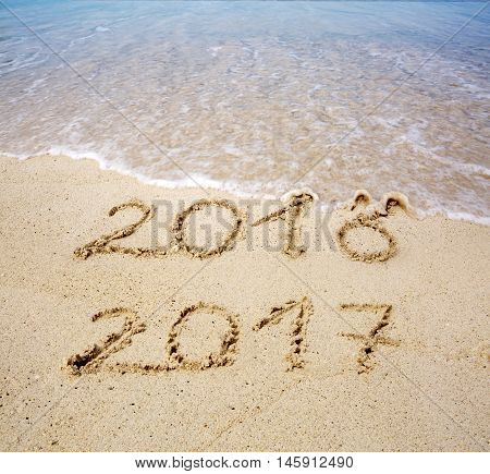 2016 2017 inscription written in the wet beach sand with sea water wave. Inscription 2016 and 2017 on a beach sand, the wave is almost covering the digits 2016.