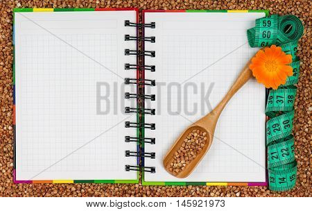 Notebook for the recipe over a buckwheat grains background with tape measure