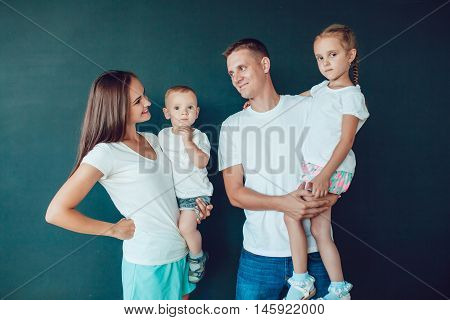 Young family of four standing in white shirt over black background