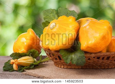 yellow pattypan squash with leaf in a wicker basket on a wooden table with a blurred background.