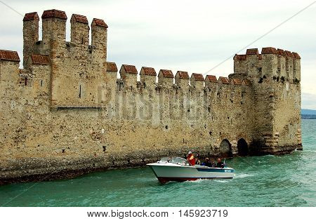 Sirmione Italy - June 1 2006: Speedboat cruises past the imposing defense walls of 13th century Scaligers' Castle (Rocca Scaligera) built over the waters of Lake Garda