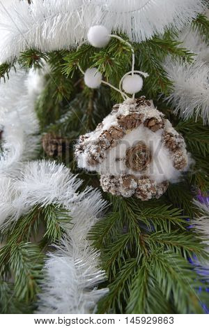 Christmas toy in the form of the house. The toy is located on a fir-tree. The house is made of fir cones and cotton