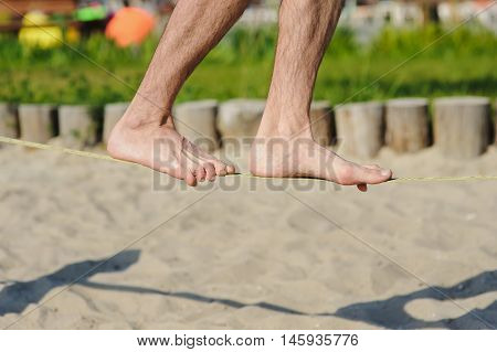 Man walking on the sling. Young man balancing on slackline at a beach.
