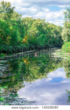 Sunny landscape of river greenwood forest and cloudy sky reflected in water