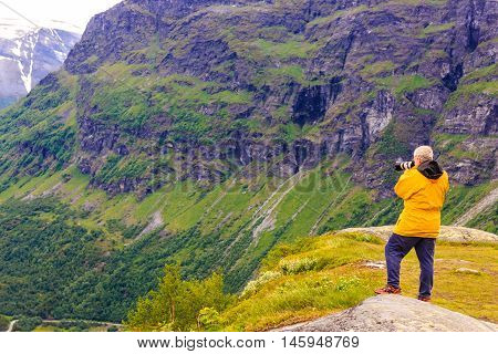 Tourism vacation and travel. Male tourist taking photo with camera enjoying mountains landscape Norway Scandinavia.