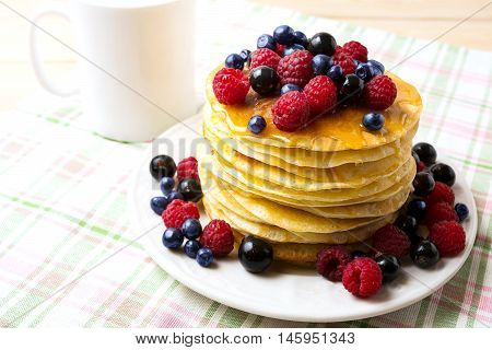 Breakfast pancakes with honey and fresh berries on the white plate and coffee mug. Homemade pancakes served with blueberry raspberry and blackcurrant.