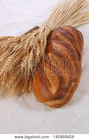 bunch of mown wheat ears with vintage handmade reaper hook sickle and rye dark white french fresh bread loaf on light linen tablecloth