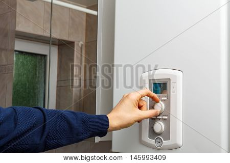 Men hand setting the temperature on control panel of DHW or central heating.