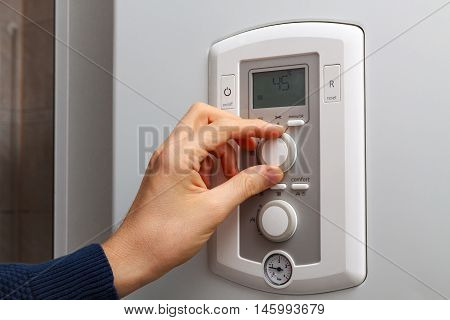 Men hand regulate temperature on 45 degree in control panel of central heating.
