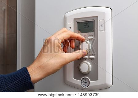 Men hand regulate temperature on 55 degree in control panel of central heating.
