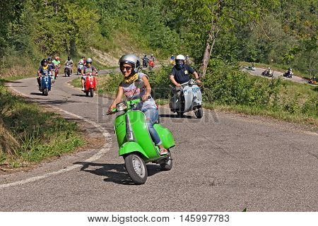 CESENA, ITALY - JUNE 26: biker girl leads a group of bikers riding a vintage italian scooter Vespa on the hills during the rally "I colli di Romagna" on June 26, 2016 in Cesena, FC, Italy
