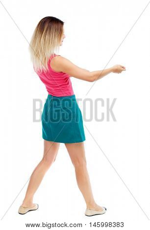 back view of standing girl pulling a rope from the top or cling to something. girl watching. Blonde in a red sweater and green skirt pulls the load on the rope.