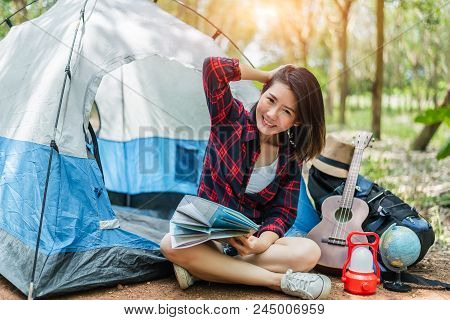 Beautiful Asian Woman Playing Ukulele In Front Of Camping Tent In Pine Woods. People And Lifestyles