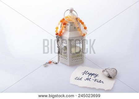 The Word Eid El Fitr   On Torn Paper Beside A Lantern And Prying Beads
