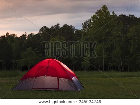 Red Roofed Tent In A Field With A Thick Treeline And Clouds At Sunset