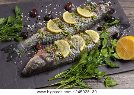 Two Seabass Fish In Marinade With Spices And Lemon, Raw Fish On Black Slate