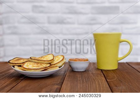 Pancakes, Fritters With Apricot Jam And Tea In Yelow Cup On The Wooden Table. White And Gray Brick B