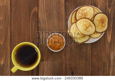 Pancakes, Fritters With Apricot Jam And Tea In Yelow Cup On The Wooden Table. White And Gray Brick B